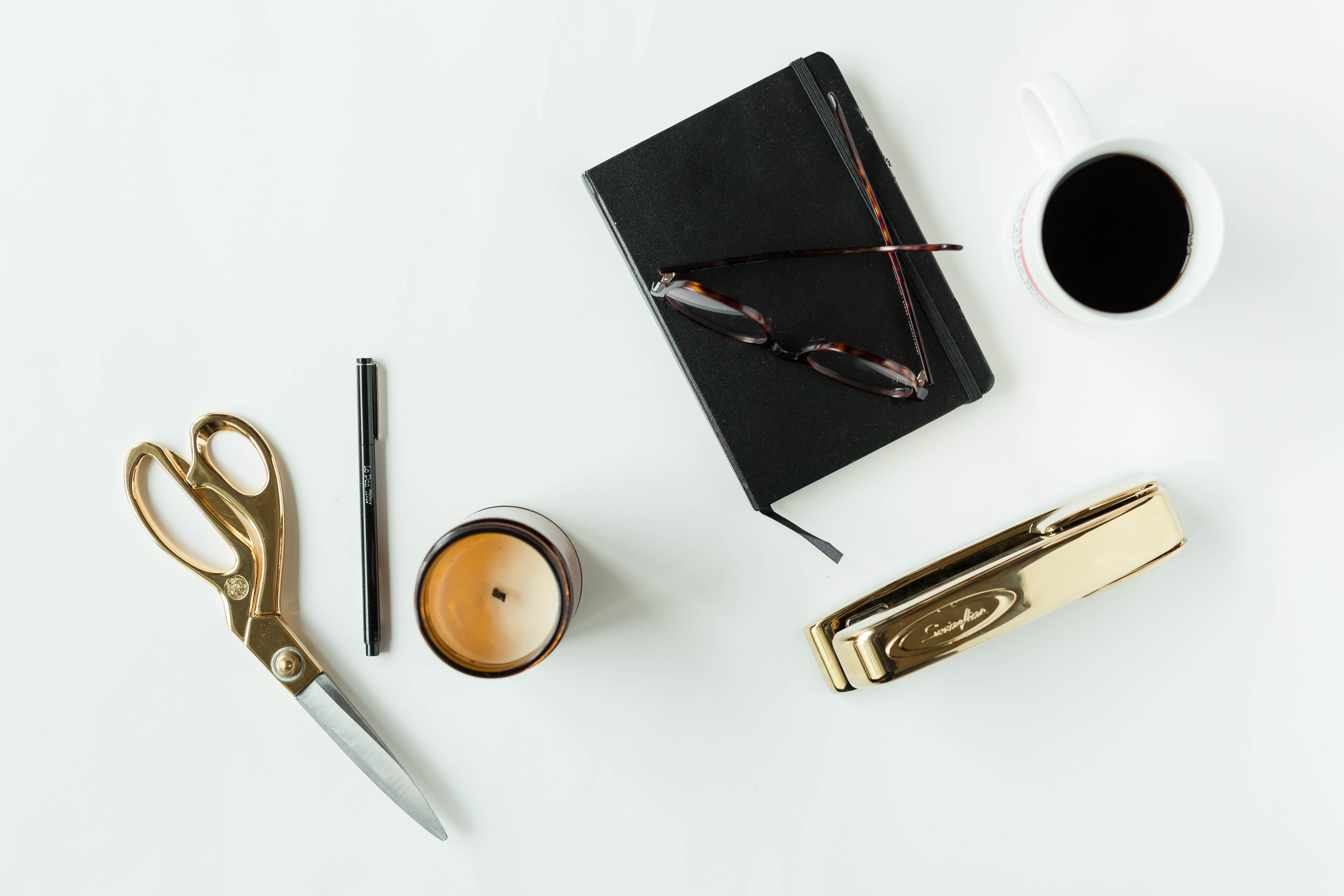 Gold scissors, journal, glasses, coffee cup, pen, gold stapler. 